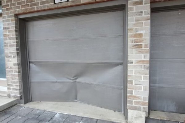 two garage doors on brick background, one of the doors has a dent from a car